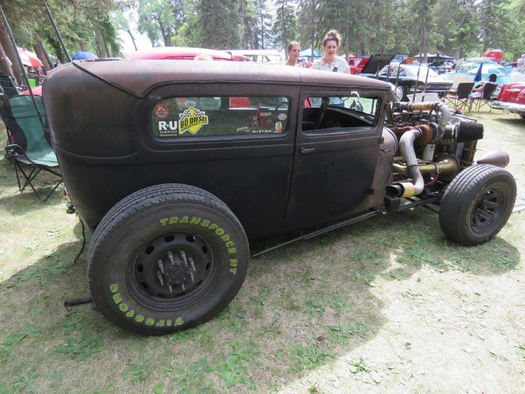 A rusty old car is parked in the grass at a car show.