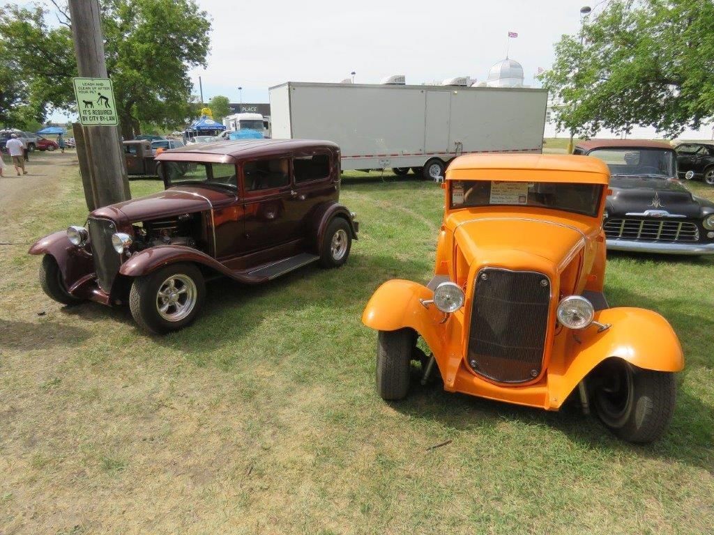 Two old cars are parked next to each other in a grassy field.