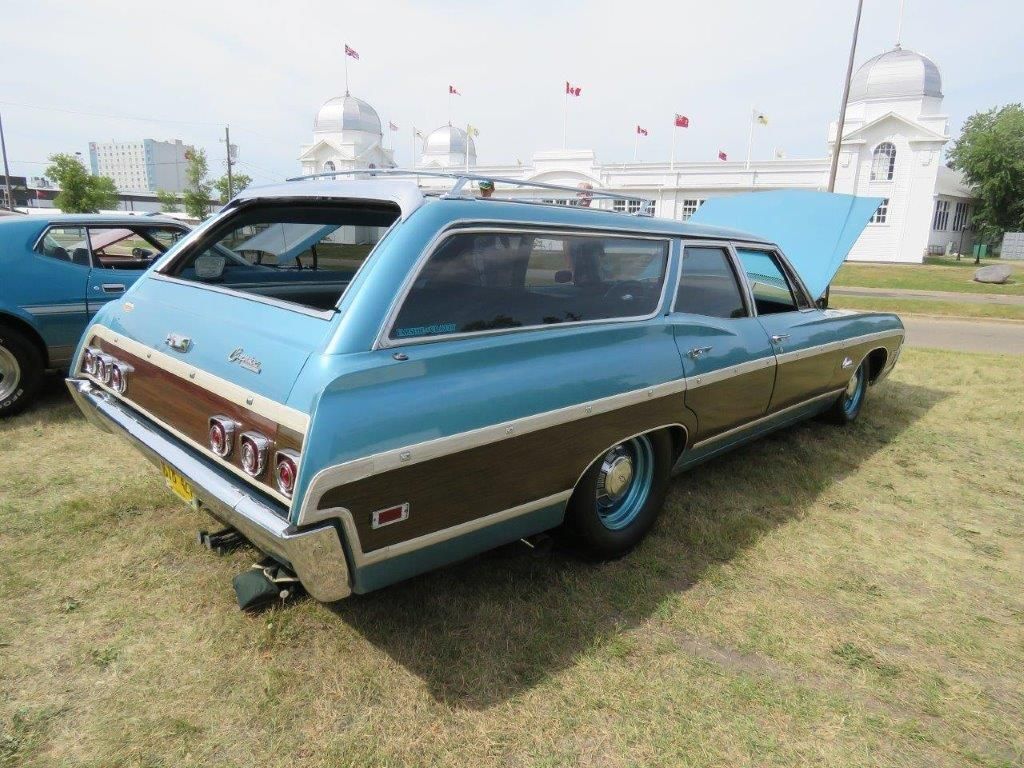 A blue and brown station wagon with the hood up is parked in the grass.