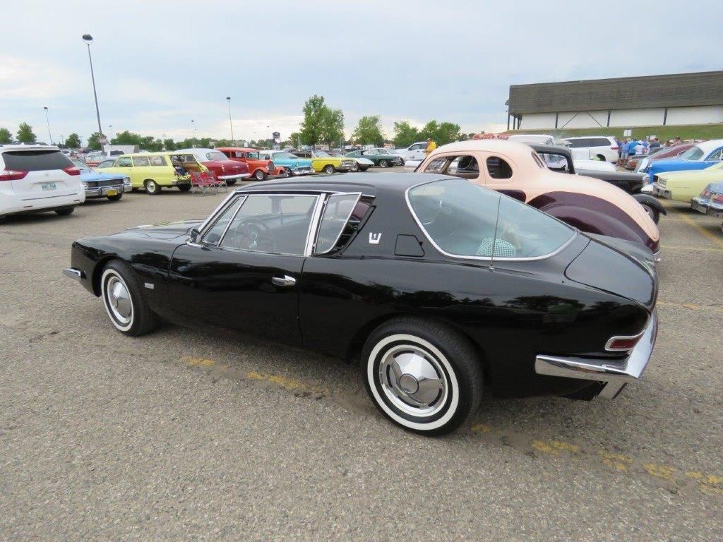 A black car is parked in a parking lot with other cars.