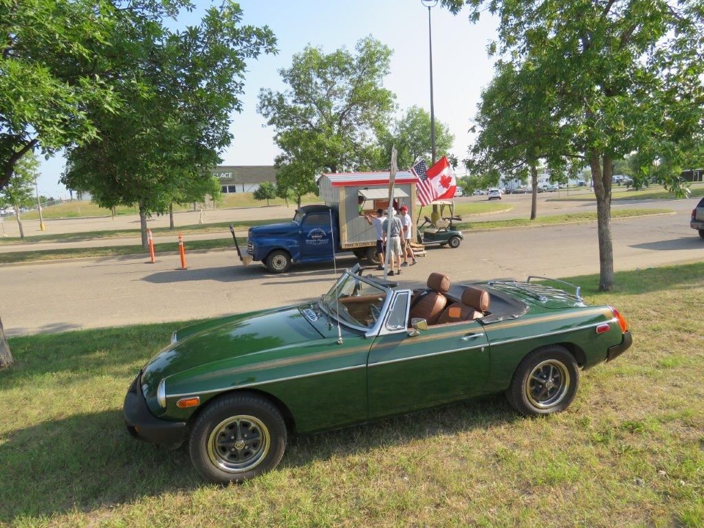 A green sports car is parked in a grassy area next to a truck.