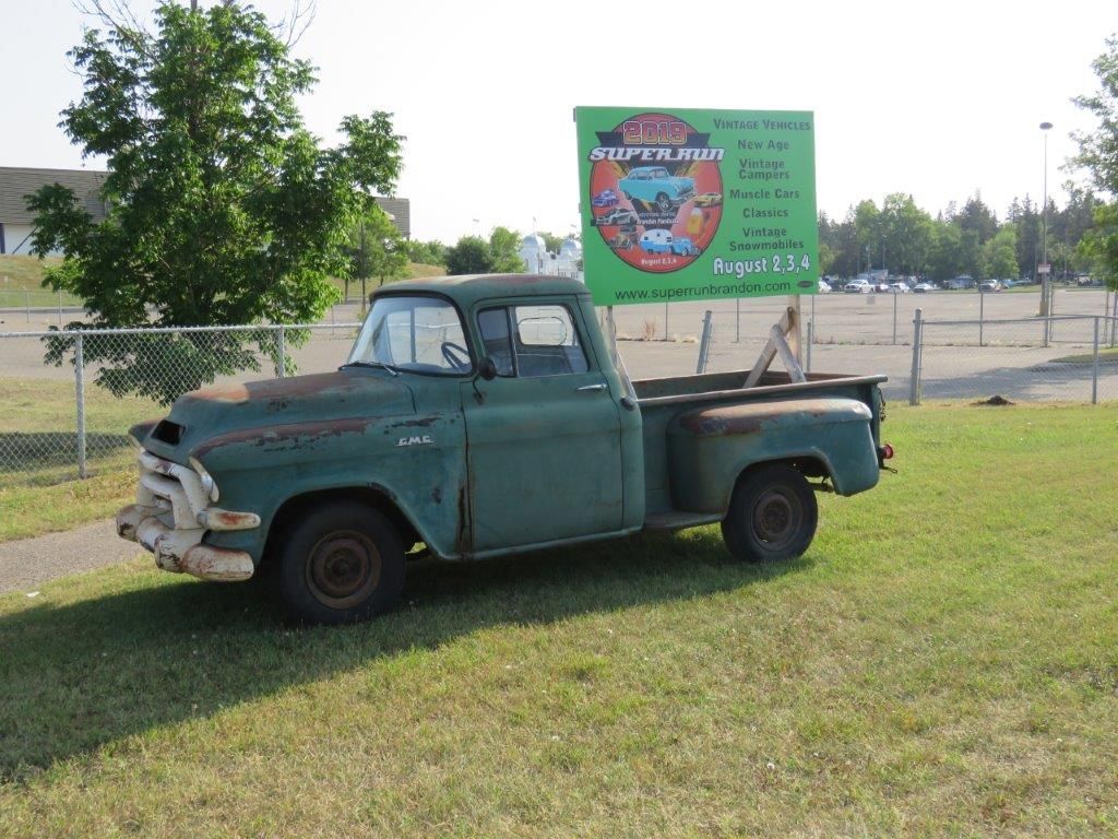 An old green truck is parked in a grassy field next to a sign.