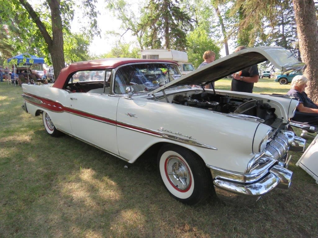 A white and red car with the hood up is parked in a grassy field.