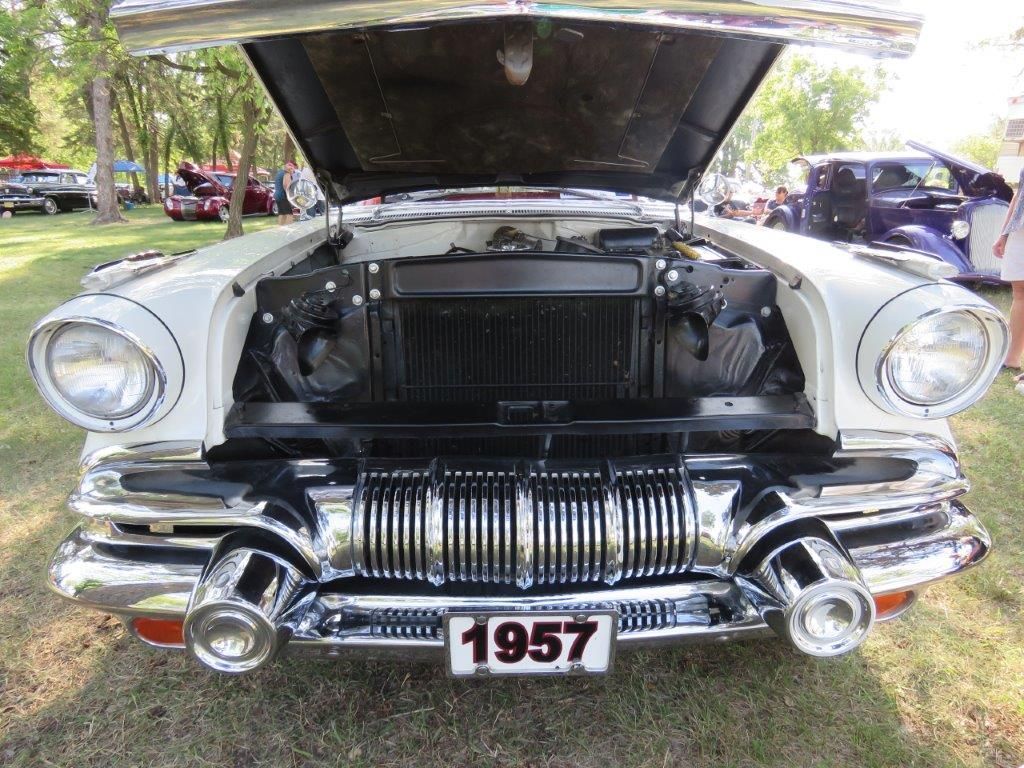A white car with the hood up and a license plate that says 1957