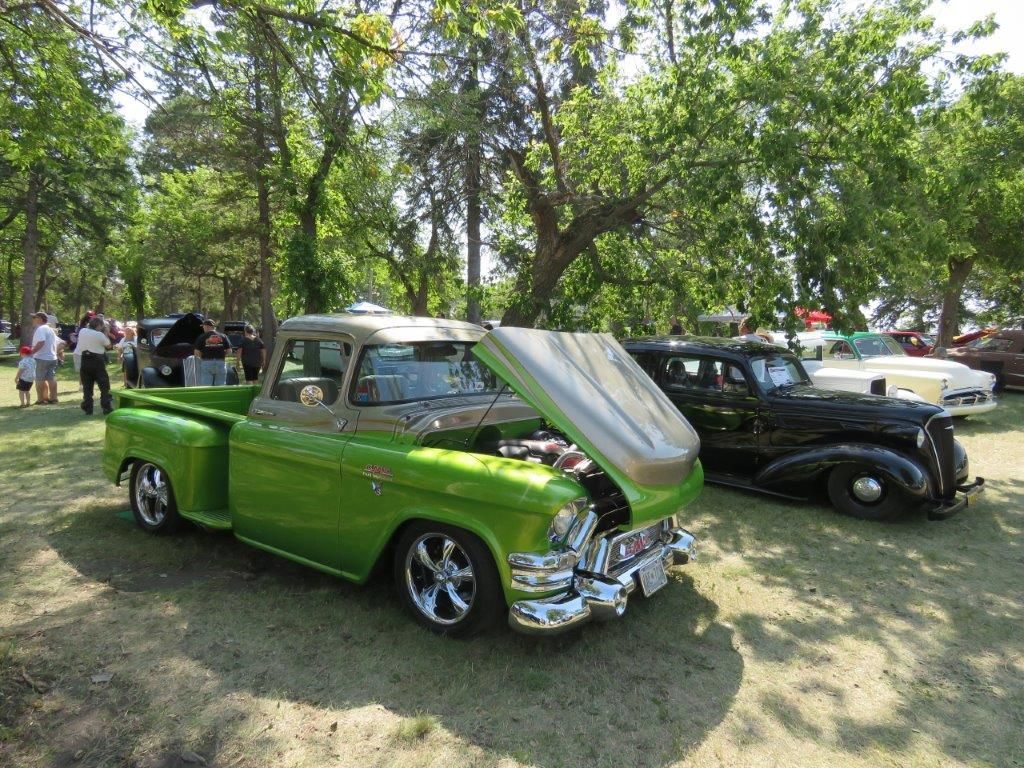 A green truck with the hood up is parked next to a black car.
