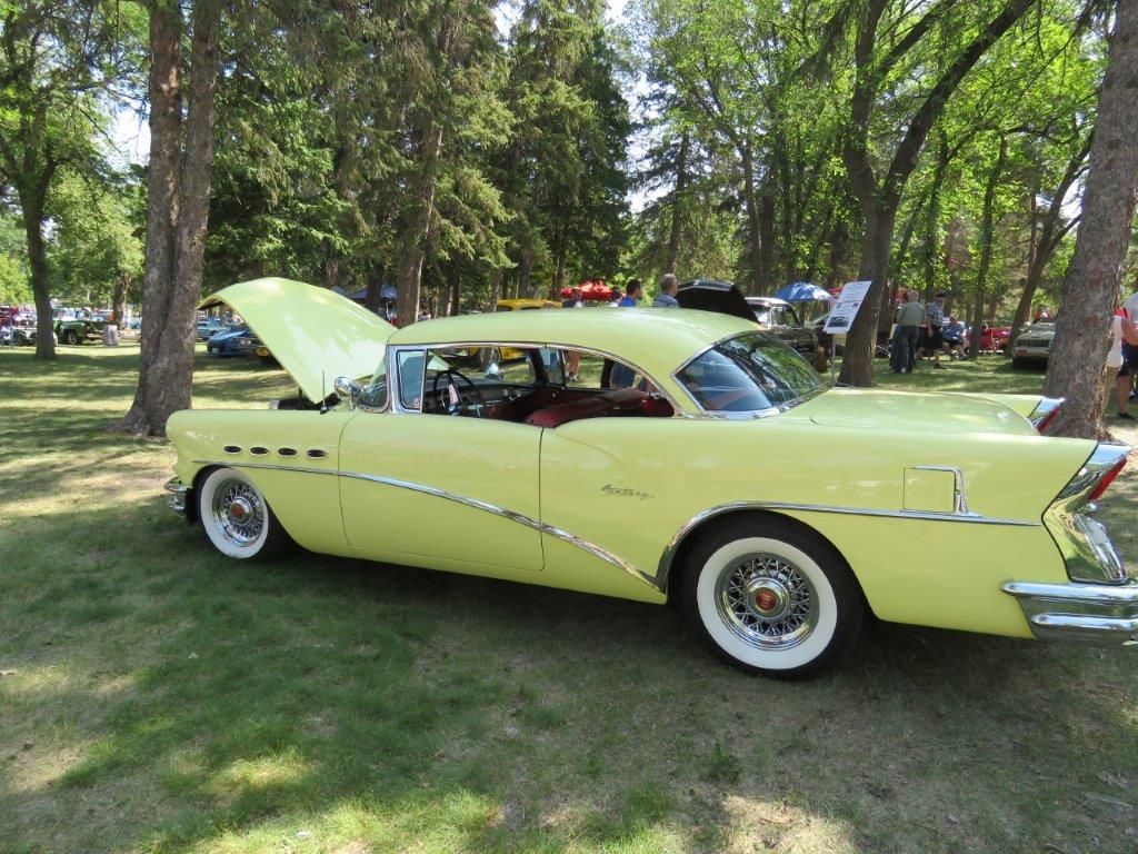 A yellow car with the hood up is parked in a park.