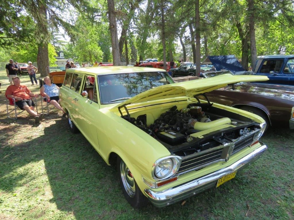 A yellow car with the hood up is parked in a grassy field.