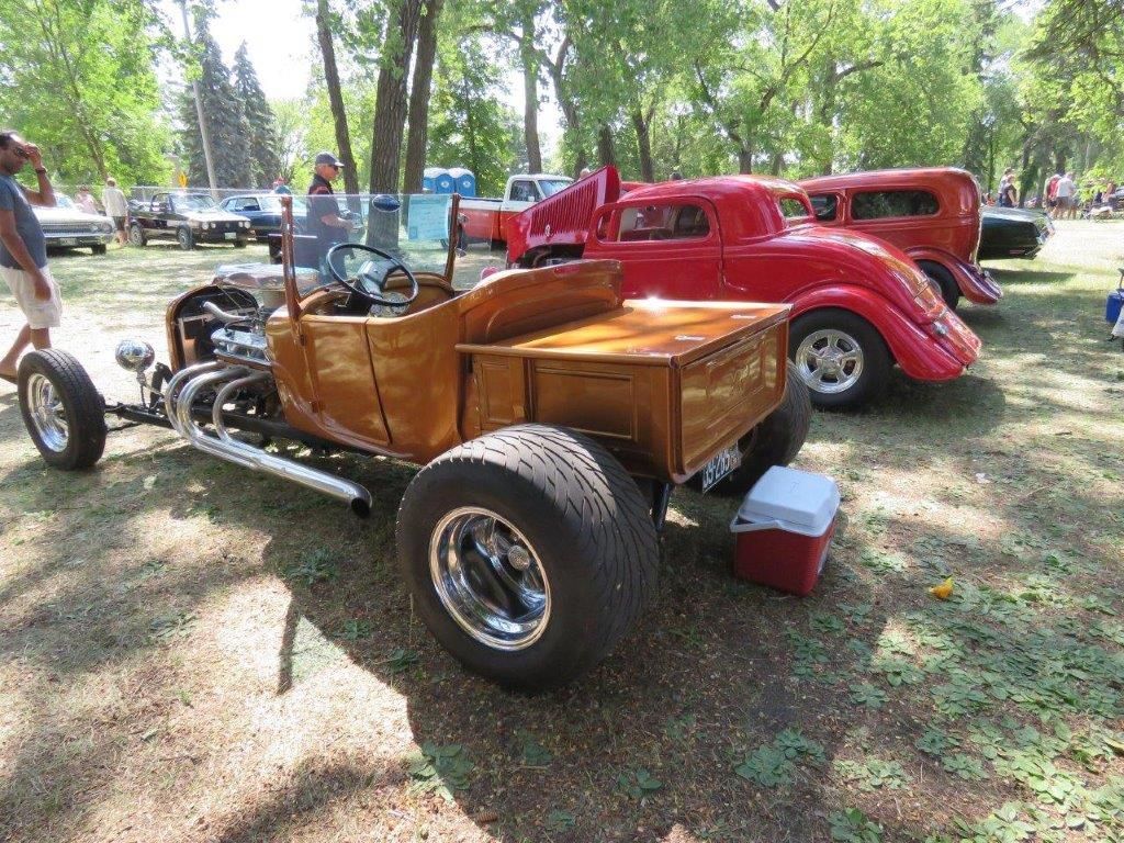A man is standing next to a wooden car with a wooden bed.