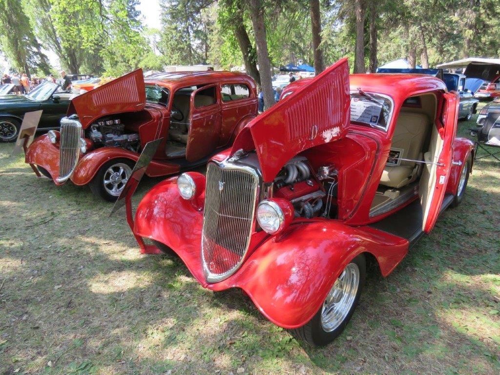 Two red cars are parked next to each other with their hoods open.