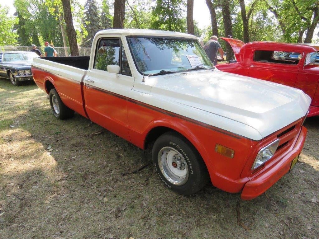 A red and white truck is parked next to a red car at a car show.