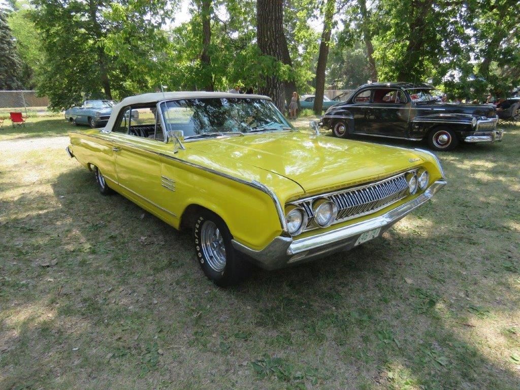 A yellow car is parked in the grass at a car show.