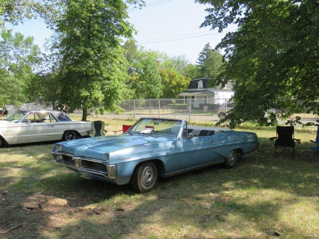 A blue convertible car is parked in a grassy field.