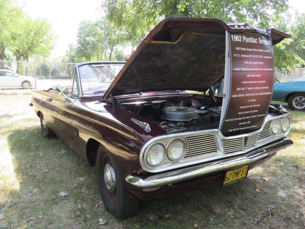 A brown car with the hood up is parked in the grass.