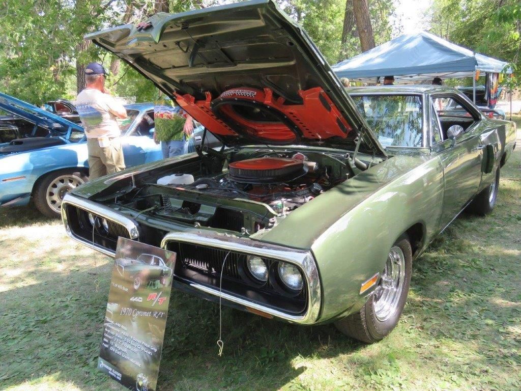 A green car with the hood up is parked in the grass at a car show.
