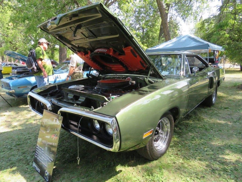 A green car with the hood up is parked in a grassy field.