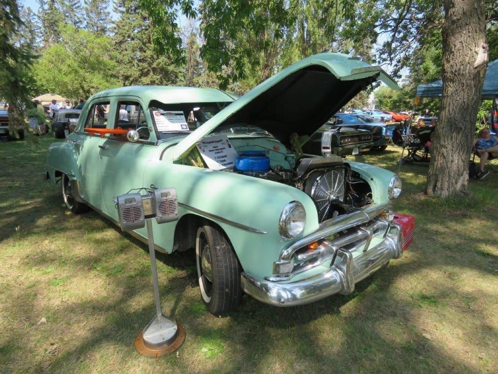 A green car with the hood up is parked in a grassy field.