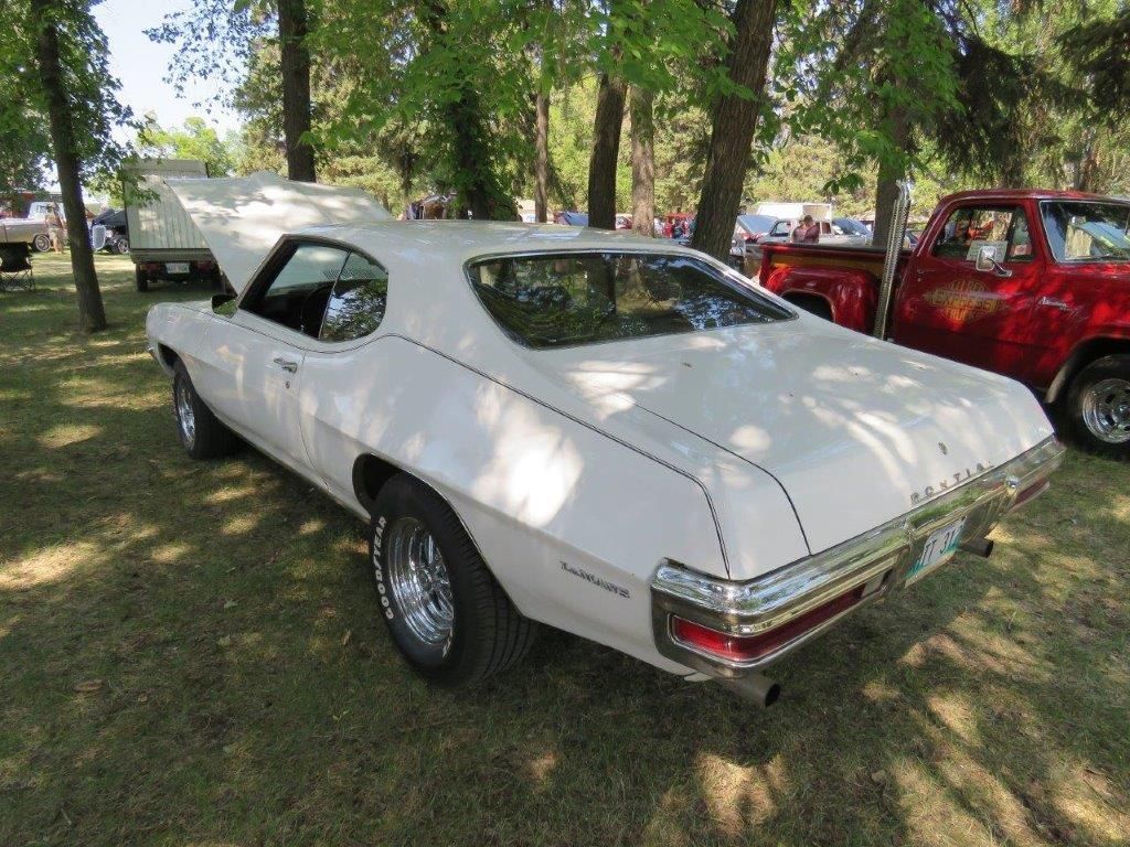 A white car with the hood up is parked in a grassy field.