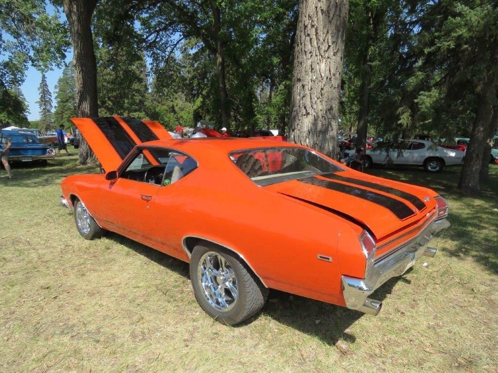 An orange car with the hood up is parked in a grassy field.