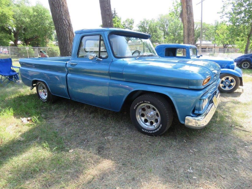 A blue pickup truck is parked in the grass next to a tree.
