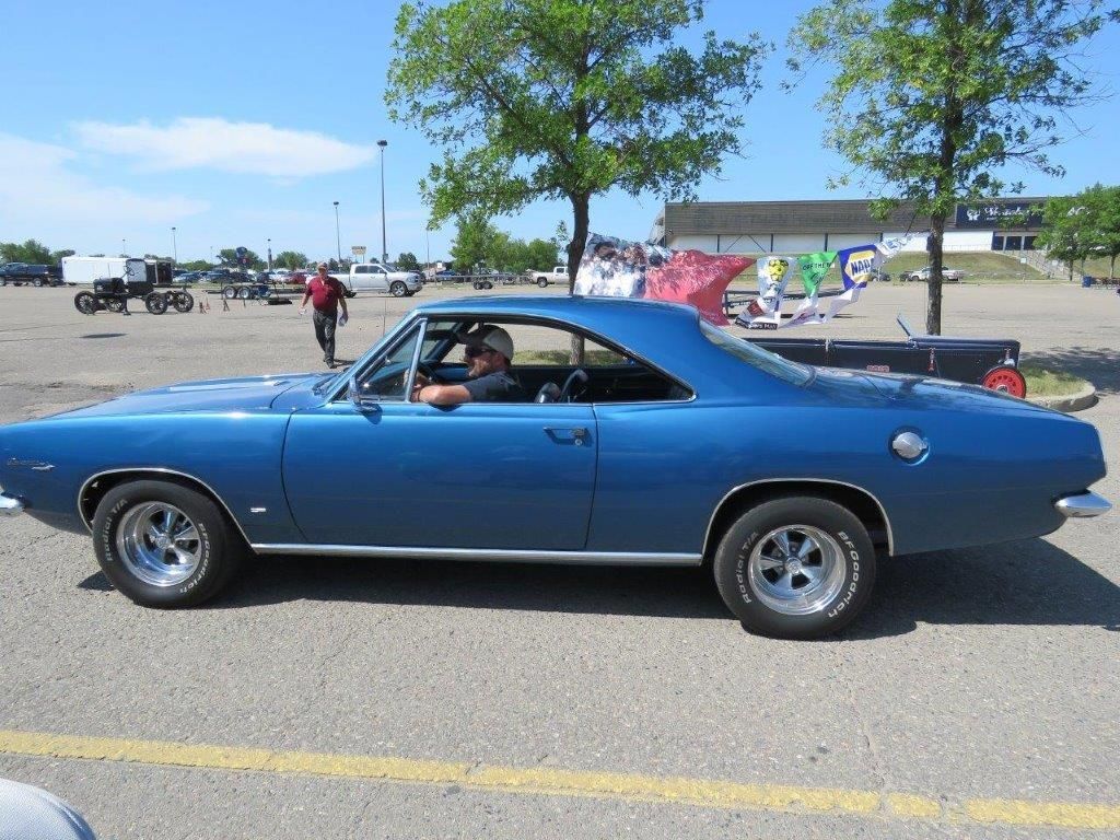 A man is driving a blue car in a parking lot