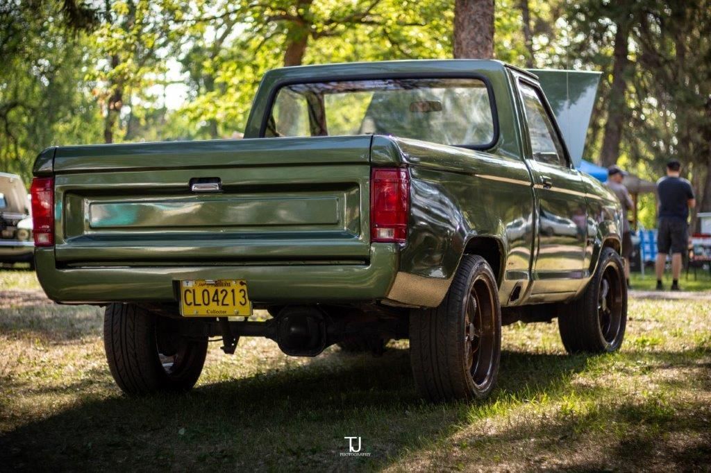A green truck is parked in the grass at a car show.