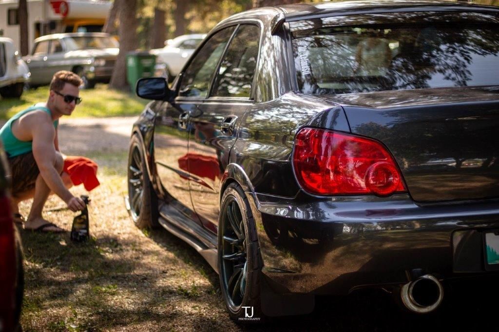 A man is cleaning a black car with a towel.