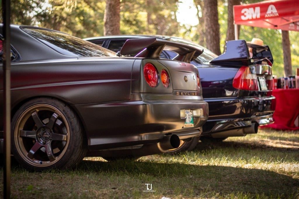 A row of cars are parked in a grassy area in front of a 3m tent.