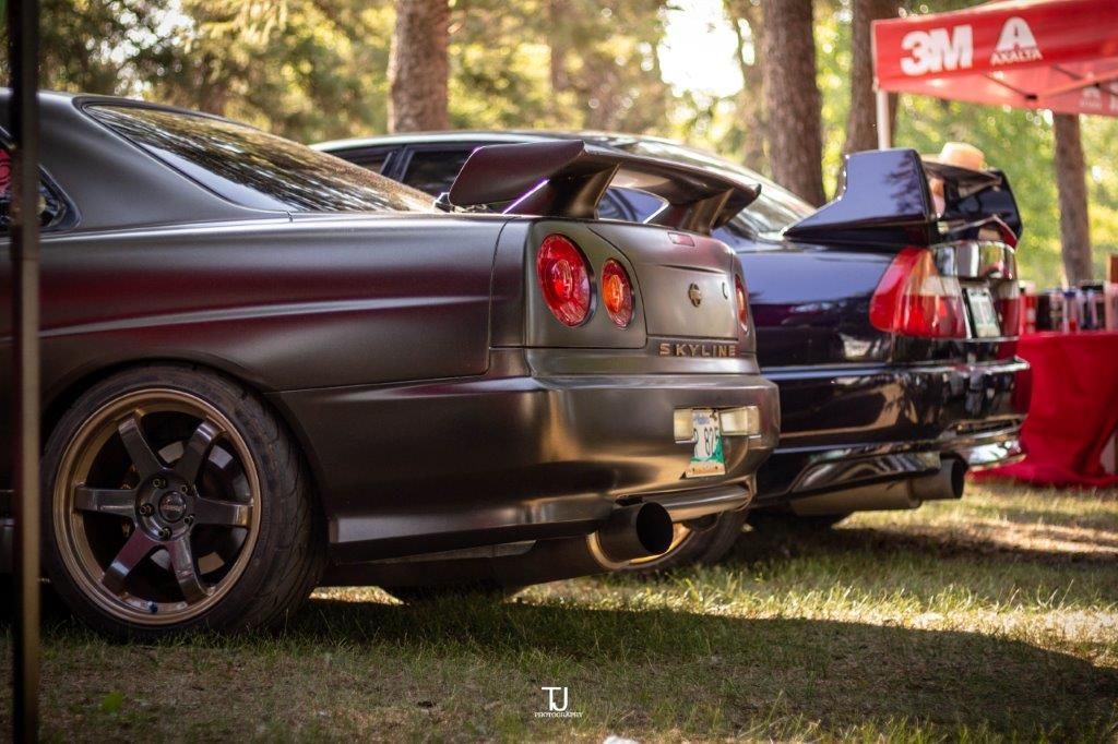A row of cars are parked in a grassy area in front of a 3m tent.