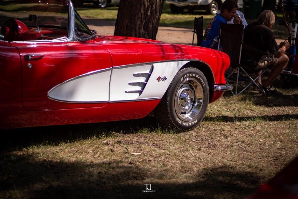 A red and white car is parked in the grass at a car show.