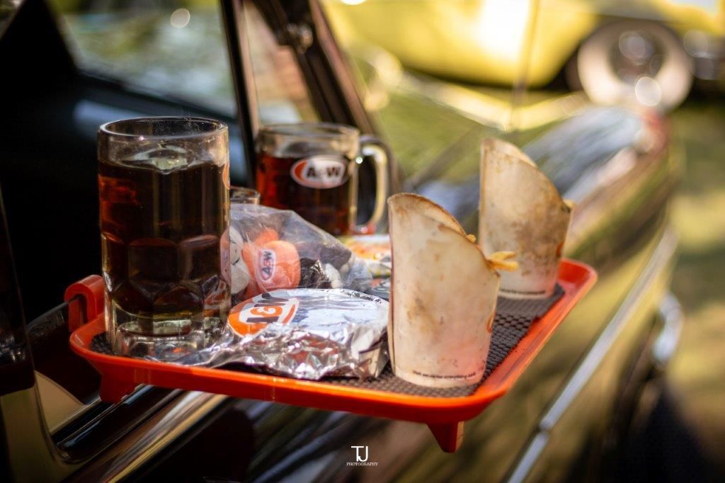A tray with two glasses of soda and a piece of bread on it is sitting on the side of a car.