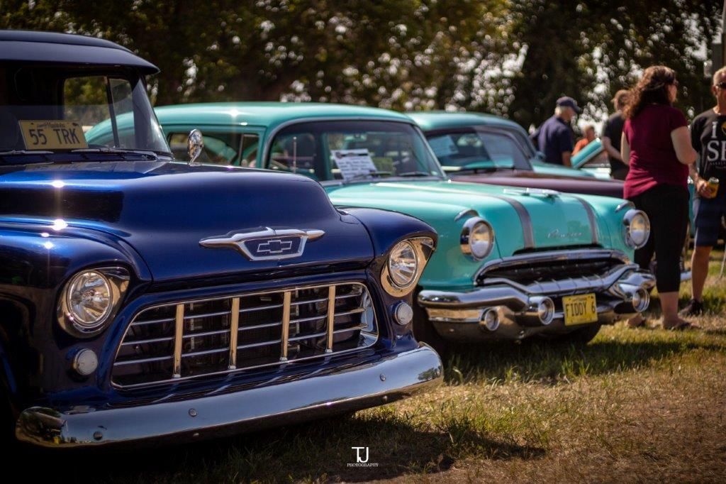 A row of old cars are parked in a grassy field.