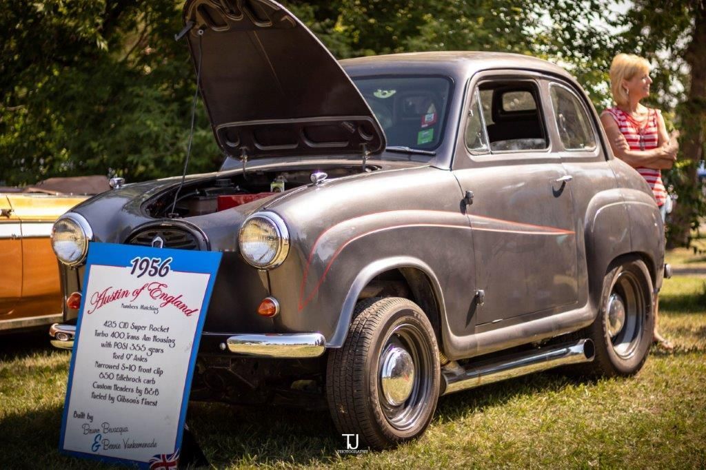 An old car with the hood up is on display at a car show.