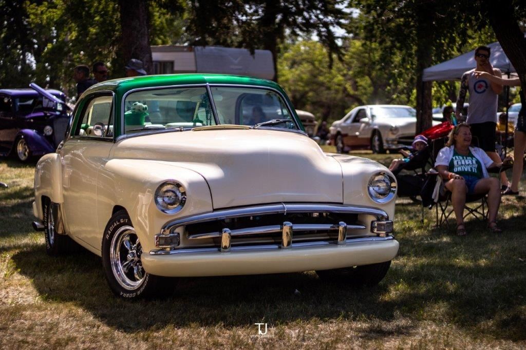 A white car with a green top is parked in the grass at a car show.