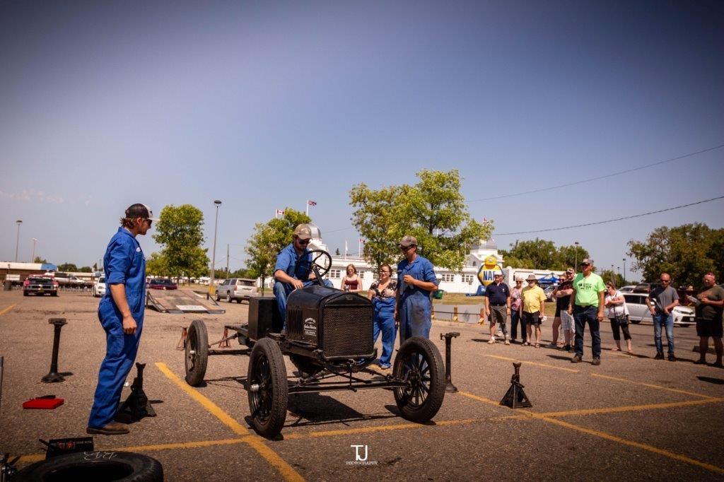 A group of men are working on an old car in a parking lot.