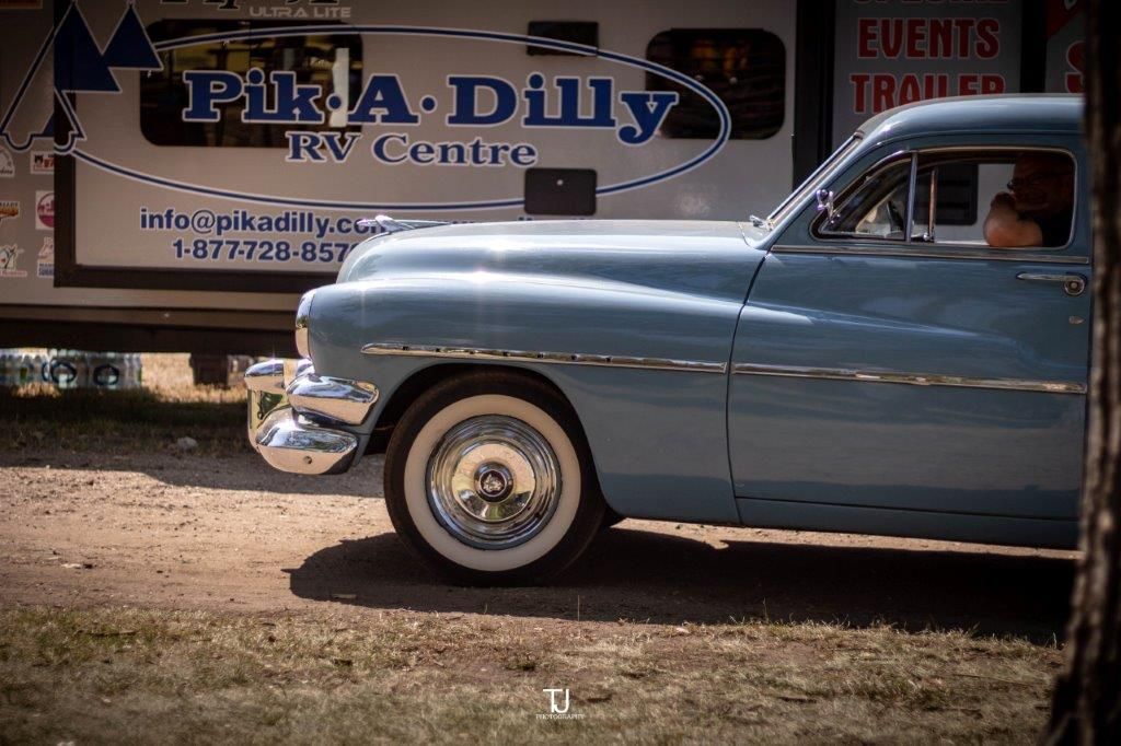 A blue car is parked in front of a pika dilly trailer.