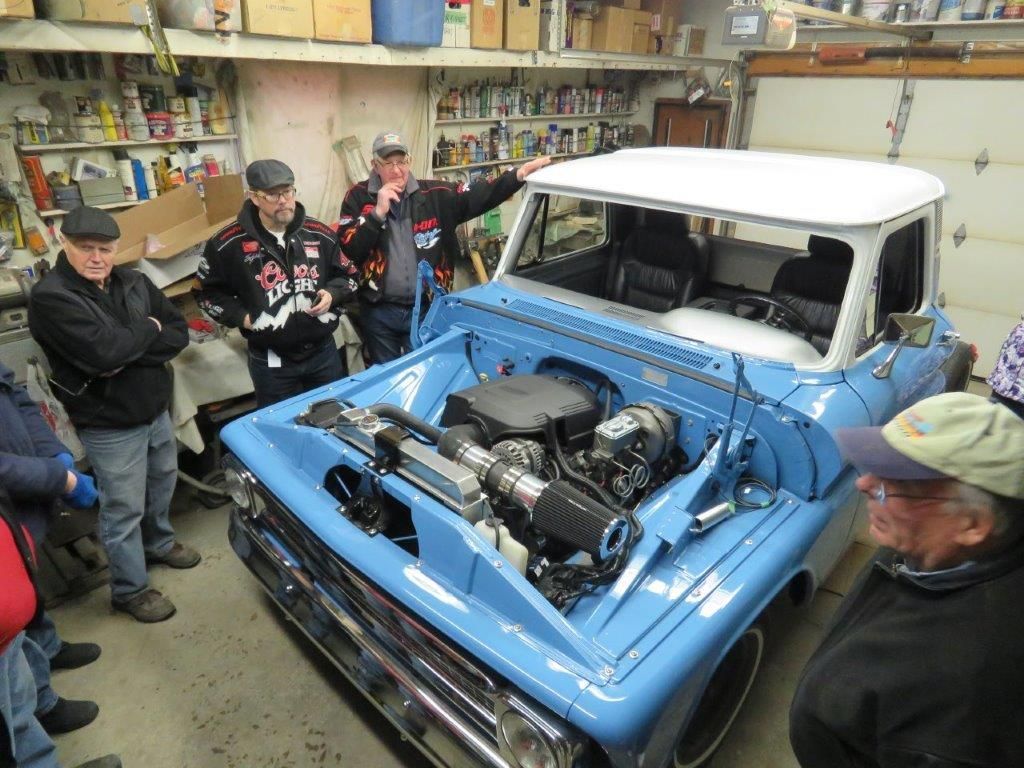 A group of men are looking at a blue truck in a garage.