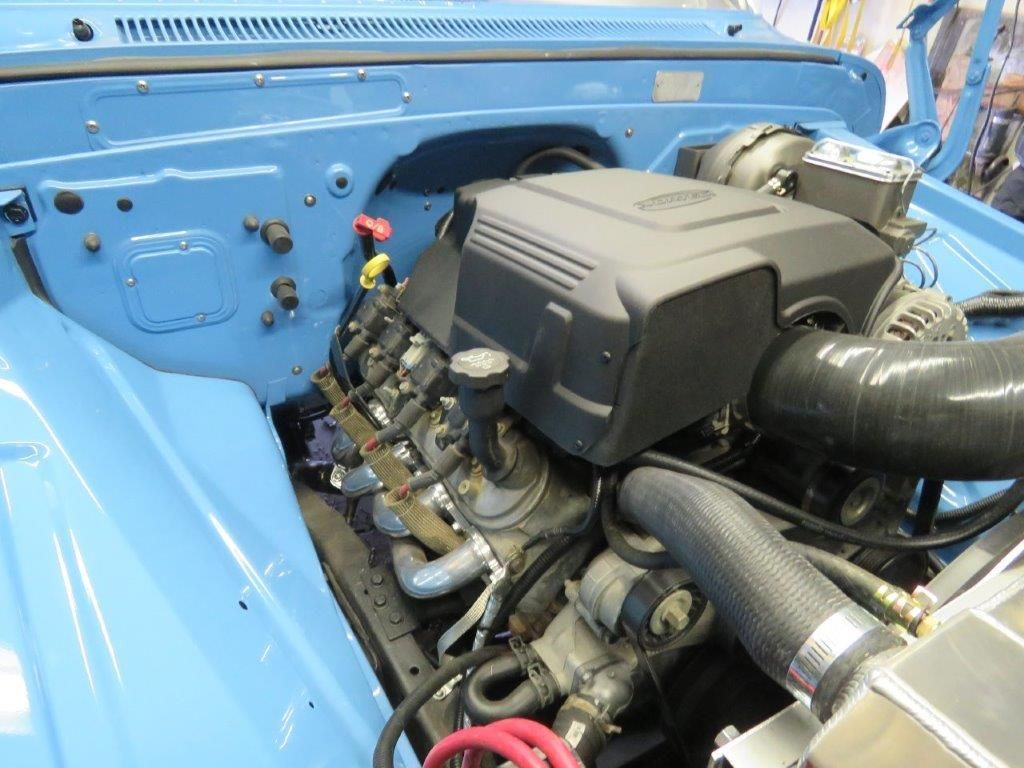 The engine of a blue truck is shown with the hood open.