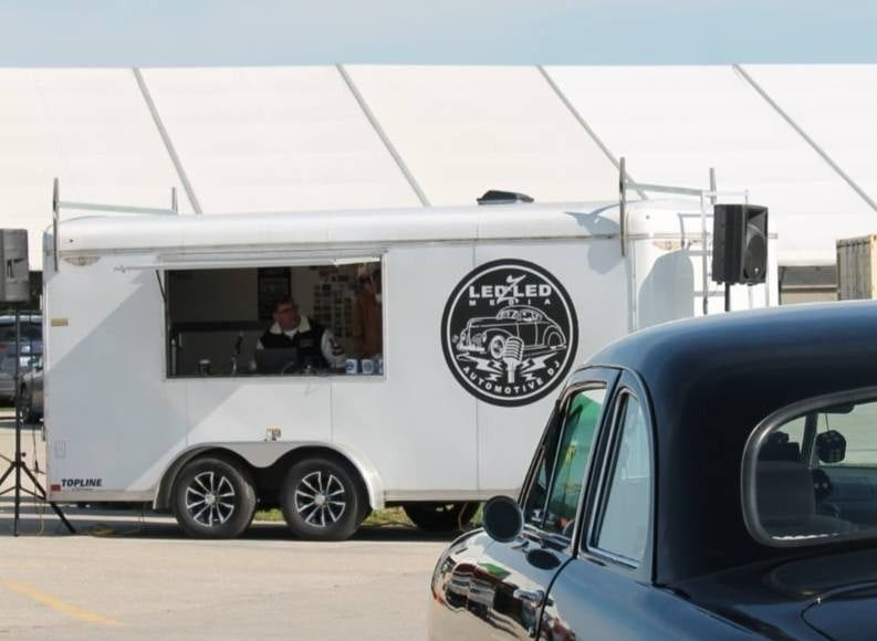 White music trailer with a logo, window open, person inside, near black car.