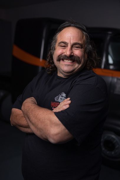 A man with dreadlocks is leaning against a purple car.