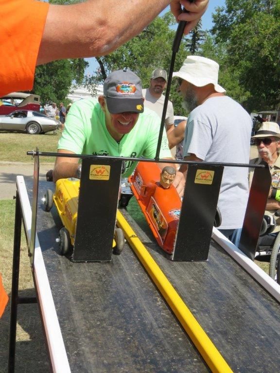 A man in an orange shirt is playing with a toy car on a track