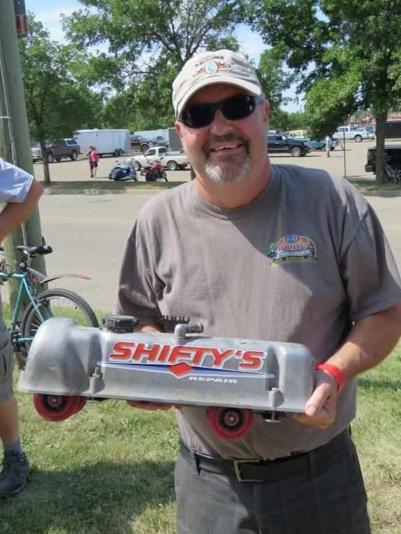A man in a gray shirt is holding a shifty 's valve cover