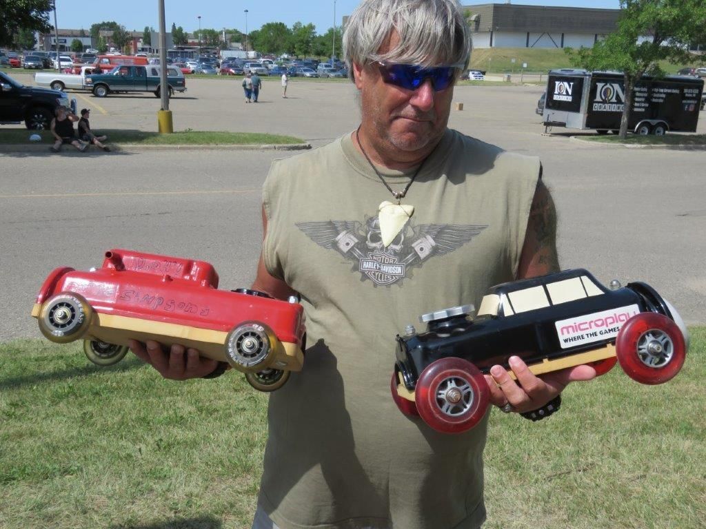 A man is holding two toy cars one red and one black