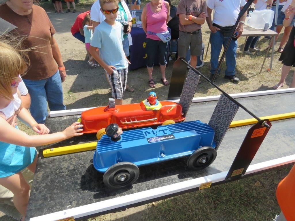 A group of people are watching a blue and red toy car race on a track