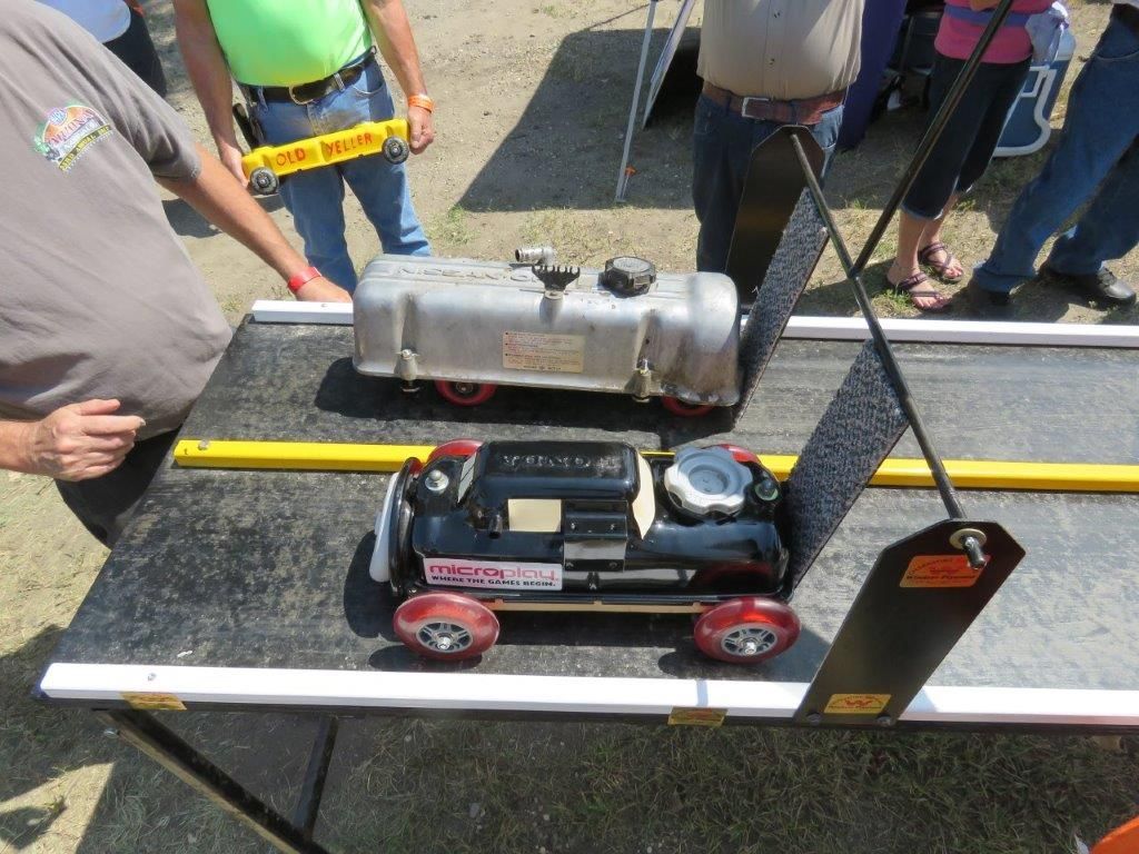 A toy car is sitting on top of a table with people standing around it