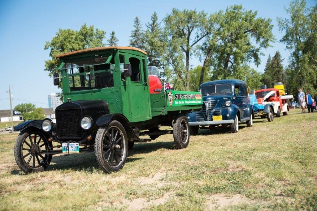 A row of old cars are parked in a grassy field.