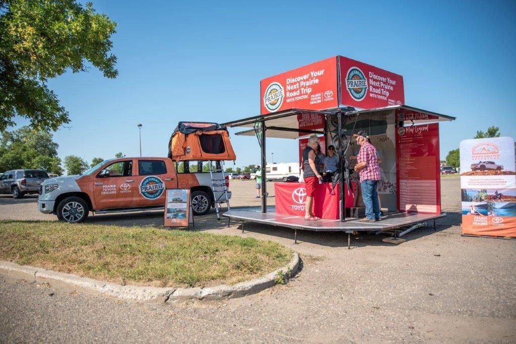 A truck with a tent on top of it is parked next to a trailer.