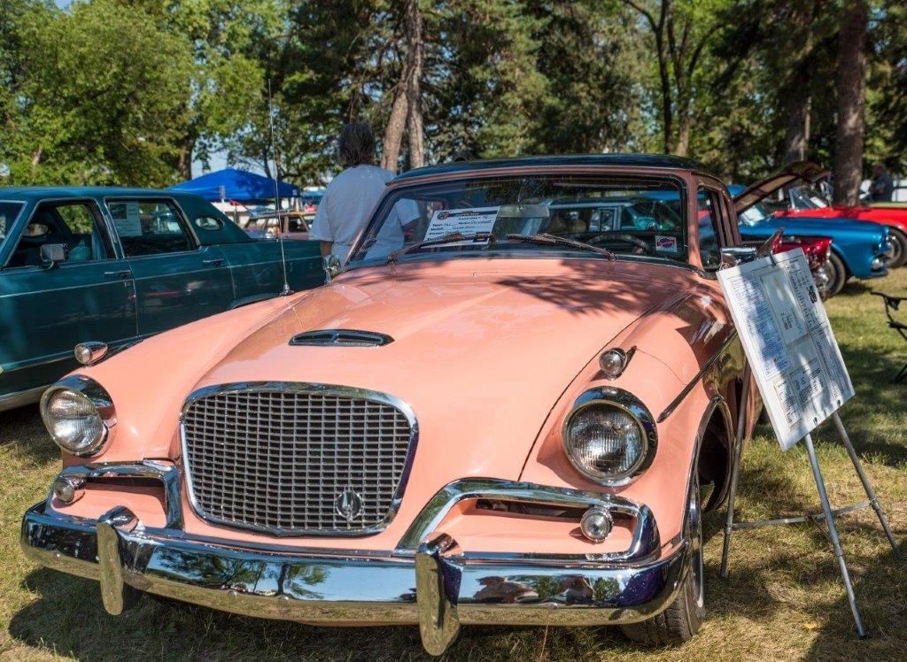 A pink car is parked in the grass at a car show.