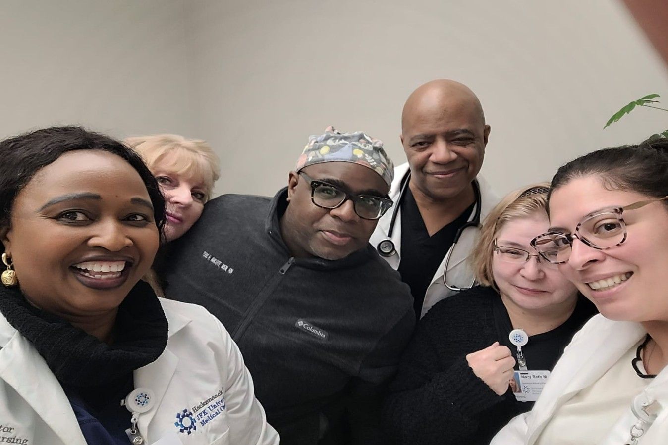 Healthcare workers smile at the camera. People of various ethnicities pose inside a medical office.