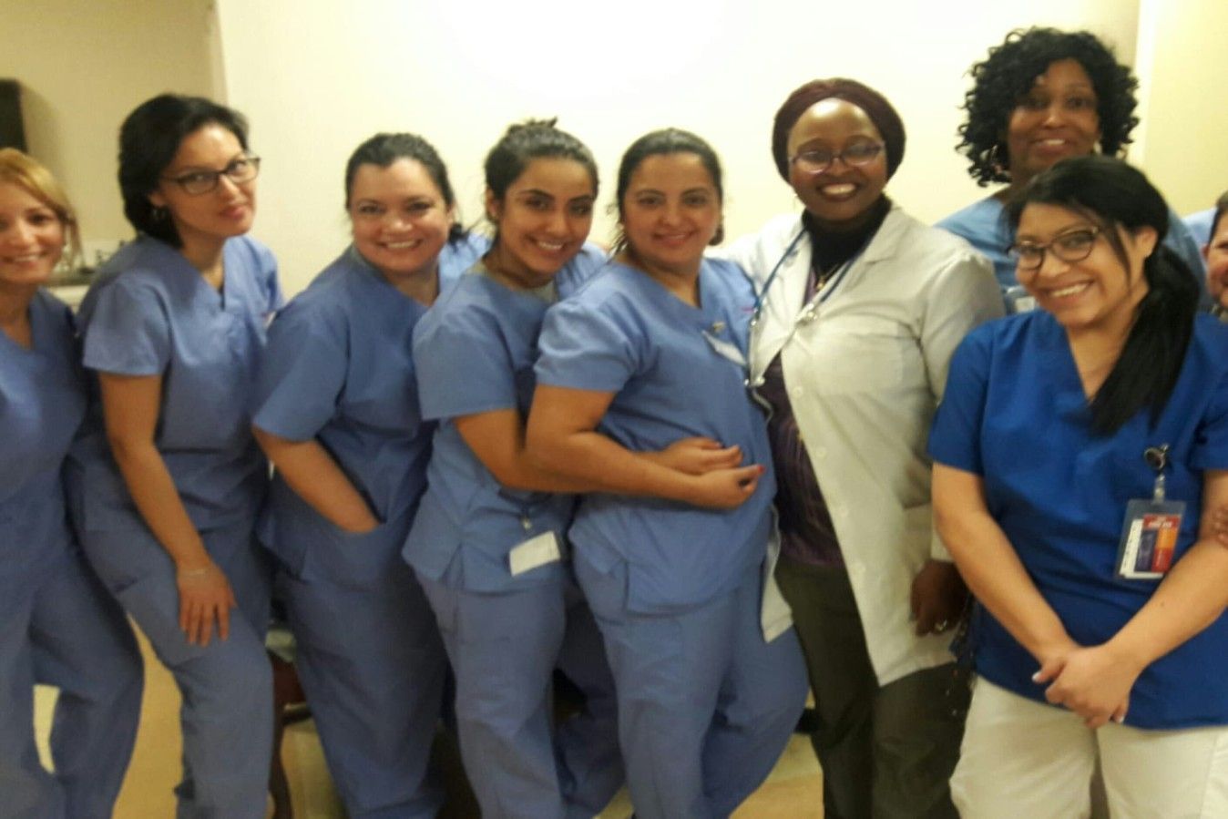 Group of nurses in blue scrubs smiling, posing indoors.