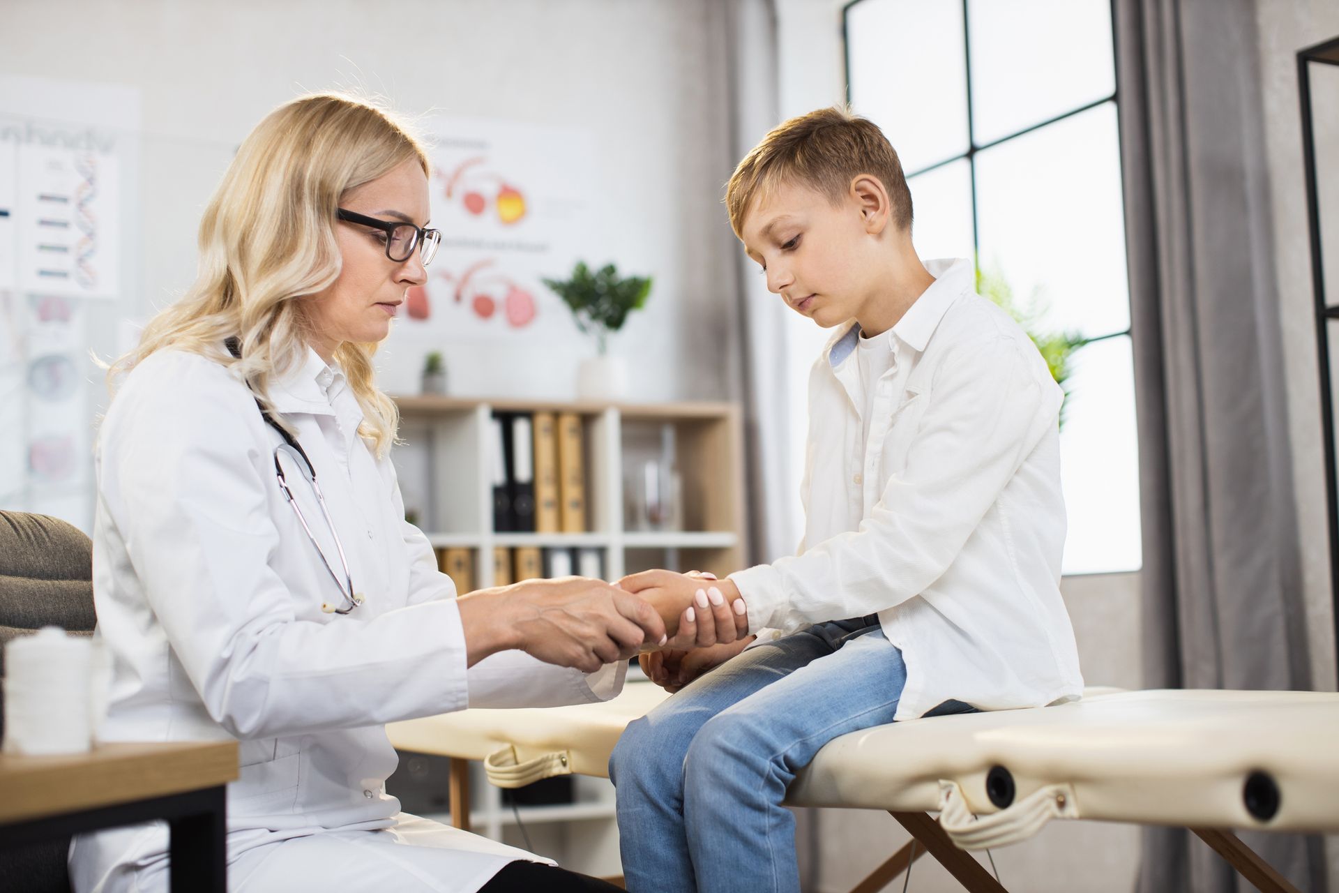 A doctor examining a young boy's wrist in a medical office.